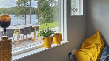 Una habitación con vistas a un lago, una mesa de comedor, sillas y plantas en macetas amarillas.