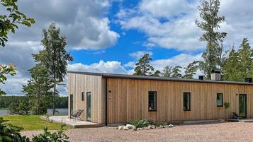 A modern wooden cabin with a gravel driveway and a lake view.