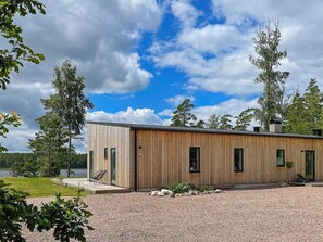 A modern wooden cabin with a gravel driveway and a lake view. - 5 Star Holiday Home in Hacksvik (Håcksvik)