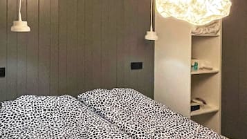 A bedroom with a bed, a hanging light fixture, and a shelf with toiletries.