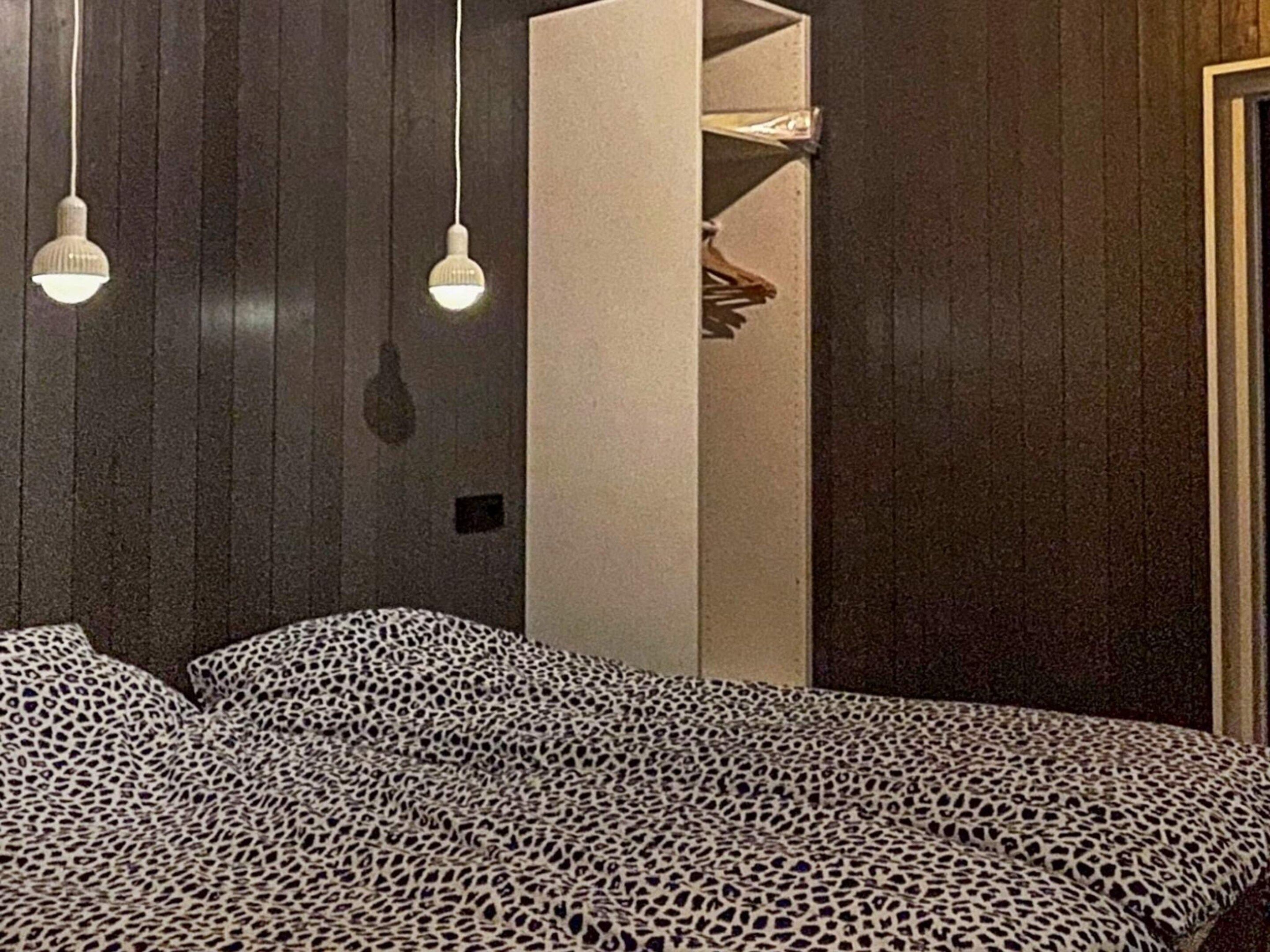 A room with a bed covered in a leopard print blanket, wooden walls, and hanging pendant lights.