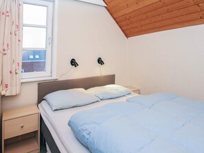 A bedroom with a bed, a nightstand, a window with curtains, and two wall-mounted lamps.