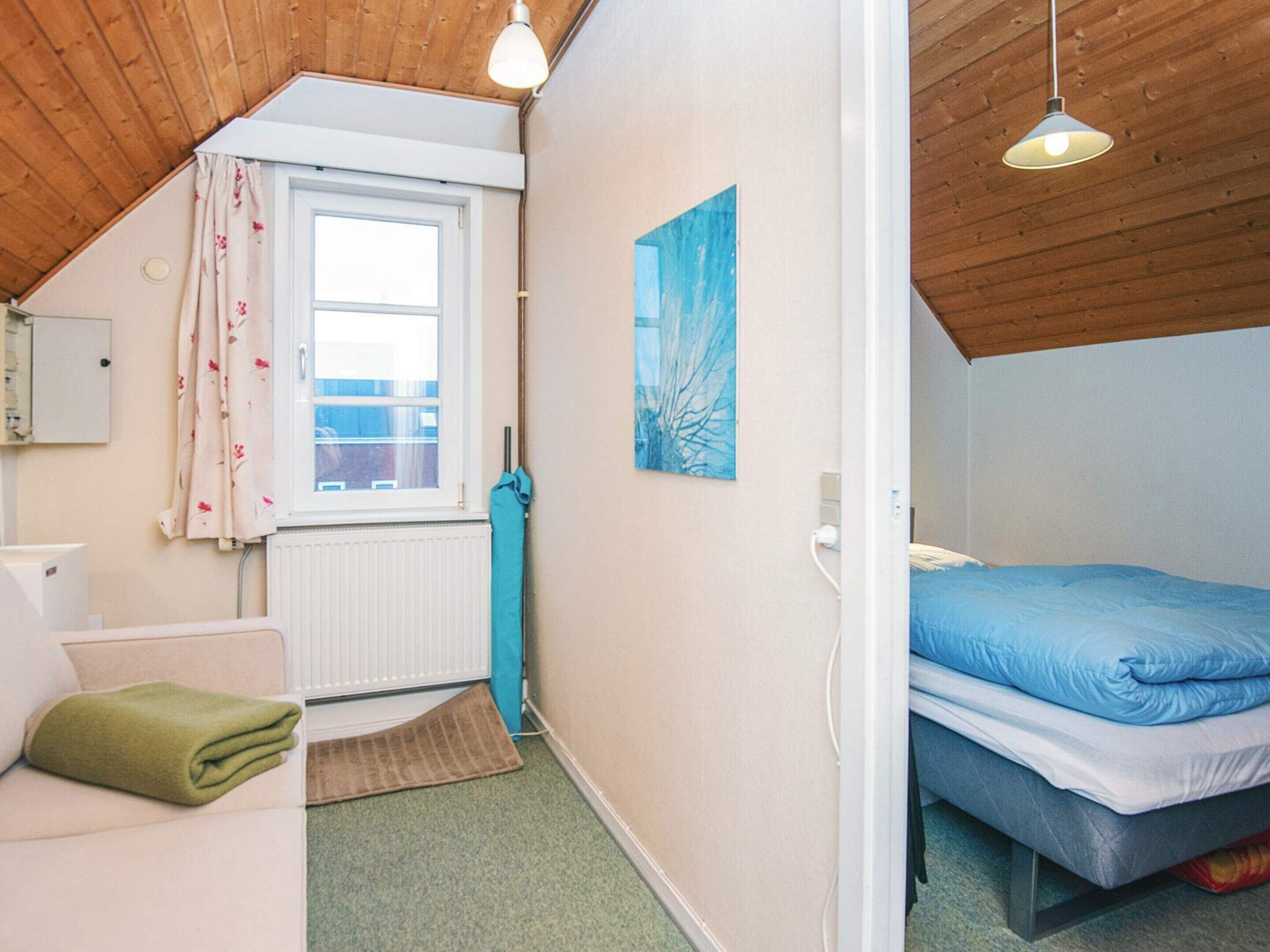 Ein kleines, gemütliches Schlafzimmer mit einem Einzelbett, einem Fenster mit Vorhängen, einem Heizkörper und einem Bild an der Wand.