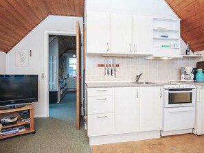 A compact kitchen with white cabinets, a built-in oven, and a sink. There's a television on a stand and a bookshelf with books.