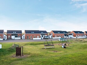 A row of red brick houses with white trim, each with a garage and a small porch. - 4 Person Holiday Home in Romo (Rømø)