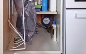 Un espace de rangement avec un sac en plastique suspendu à un portant, un récipient bleu et une armoire blanche.