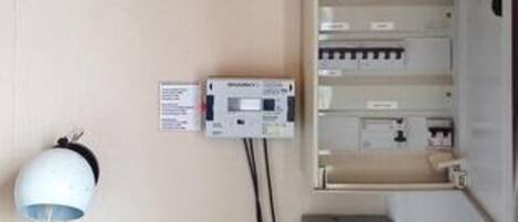 Een wandpaneel met elektrische installatie, een bedieningspaneel en een wit apparaat, mogelijk een thermostaat, verbonden door bedrading.