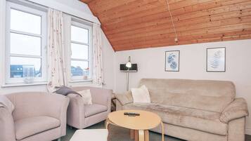 A cozy living room with a wooden ceiling, two sofas, a round coffee table, and a TV on a stand.