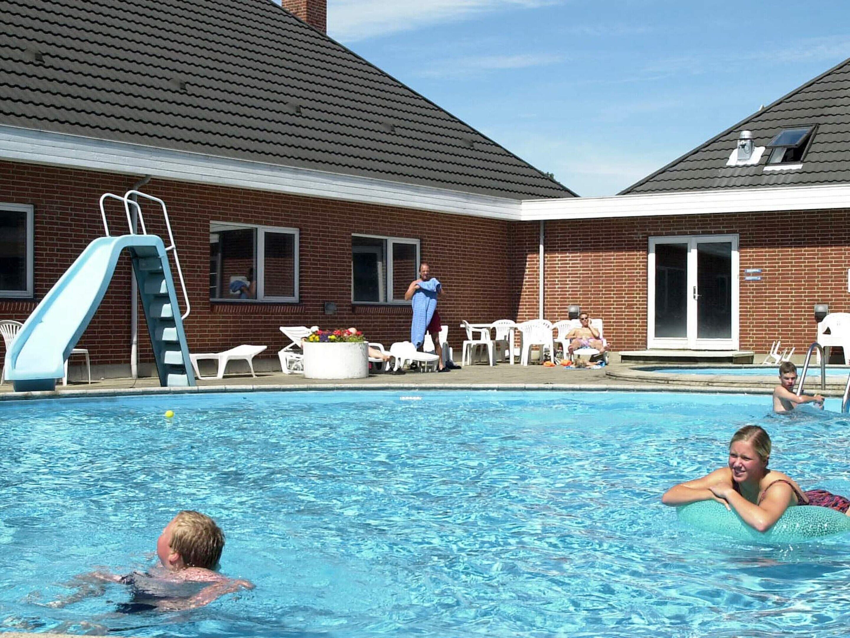 Ein Schwimmbecken mit Rutsche, Liegestühlen und einem Backsteinhaus im Hintergrund.