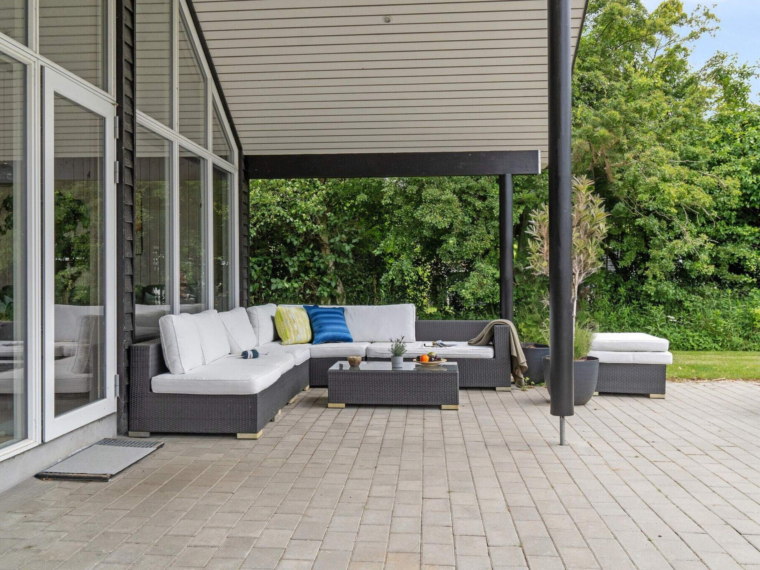 A covered outdoor seating area with a sofa and coffee table, a small table with fruits, and a bench.