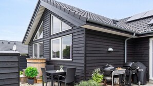 A modern house with a patio area featuring a grill, outdoor seating, and potted plants. - 5 Star Holiday Home in Jaegerspris (Jægerspris)