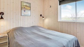 A bedroom with a bed, a nightstand, a lamp, a painting, and a window.