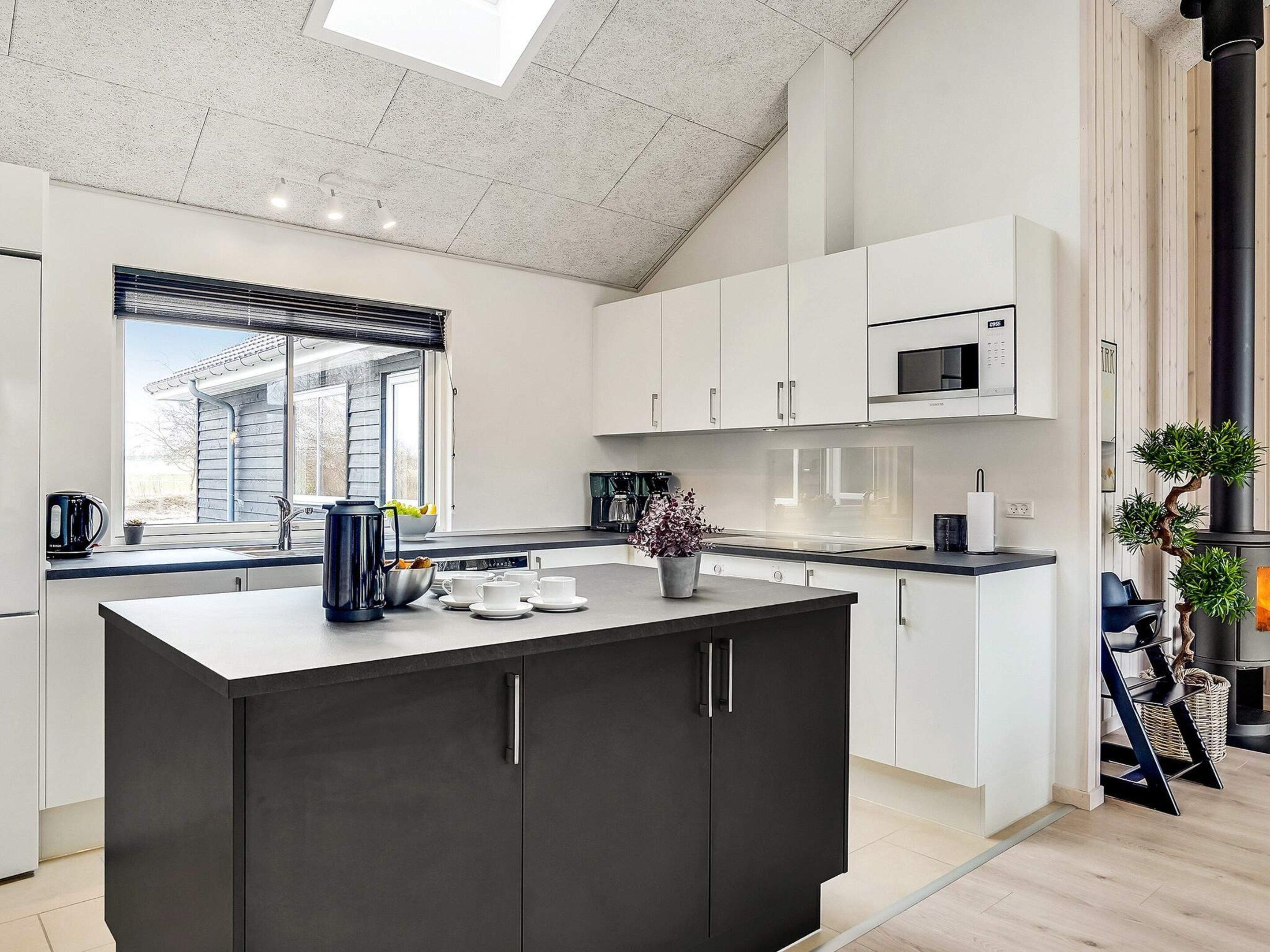 Cozinha moderna com ilha central, armários brancos e bancada preta.
