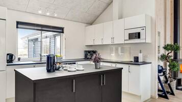 Cozinha moderna com ilha central, armários brancos e bancada preta.