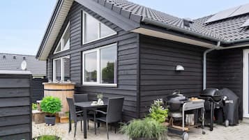 Uma casa moderna com um pátio que inclui churrasqueira, móveis de exterior e plantas em vasos.