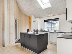 Una cocina moderna con una isla central, paredes de paneles de madera, un tragaluz y una ventana con persianas.