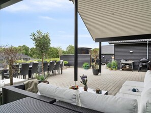 Une terrasse extérieure dotée d’un espace salon abrité, d’un barbecue et de plantes en pot.