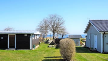 A row of cabins with a grassy yard, a small bush, and a clear view of the water in the background.
