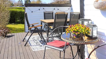 En udendørs terrasse med et bord, stole, en plantekasse og lyskæder.