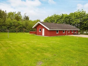 A red building with a sloped roof, a door, and windows, situated in a grassy area with trees in the background. - 5 Star Holiday Home in Nordborg (Nordborg)