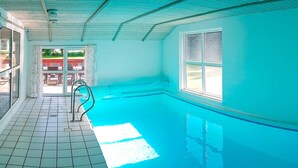 Una piscina interior con suelo de baldosas, una escalera metálica y un ventanal.