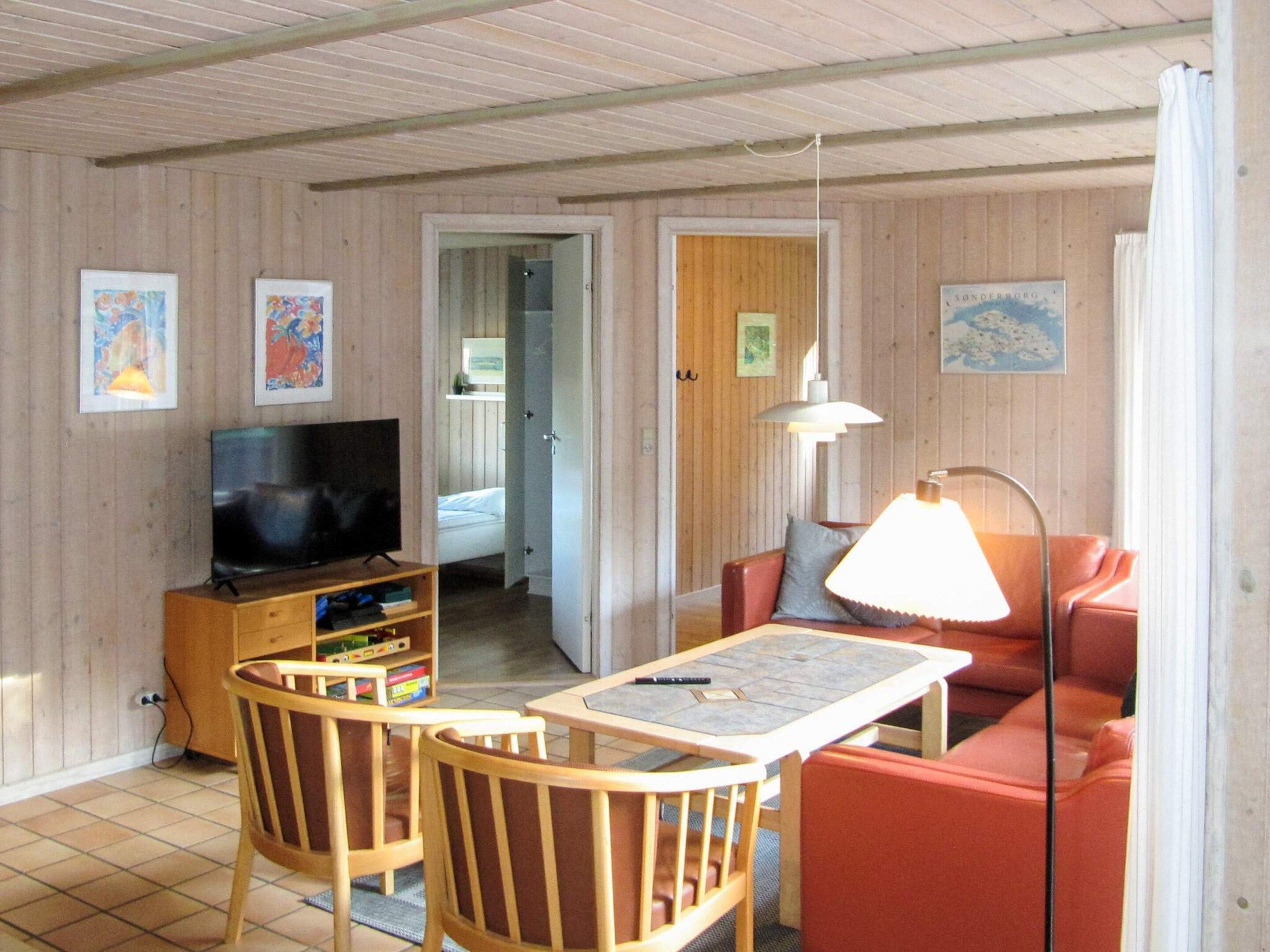 A room with a television, a table, two chairs, a sofa, and a lamp.
