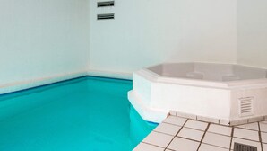 Une piscine avec un jacuzzi, un sol carrelé et un plafond avec des poutres en bois.