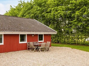 A red building with a tiled roof, a gravel driveway, and a table with chairs outside.
