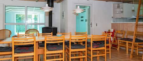 A dining area with wooden chairs and a table, a black stove, and a window with a view of greenery.