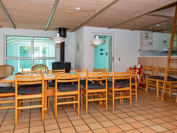 A dining area with wooden chairs and a table, a black stove, and a window with a view of greenery.