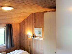 A room with wooden walls, a bed, a window with curtains, and a wall-mounted light fixture. - 5 Star Holiday Home in Nordborg (Nordborg)