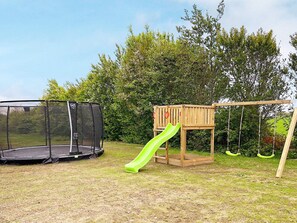 A playground with a trampoline and a wooden play structure with a slide. - 5 Star Holiday Home in Sydals (Sydals)