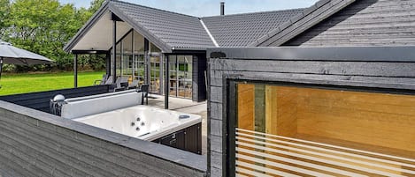 A modern building with a large outdoor hot tub, a covered seating area, and a glass enclosure.