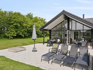 A modern outdoor patio with a glass enclosure, seating area, and a small table. - 5 Star Holiday Home in Sydals (Sydals)