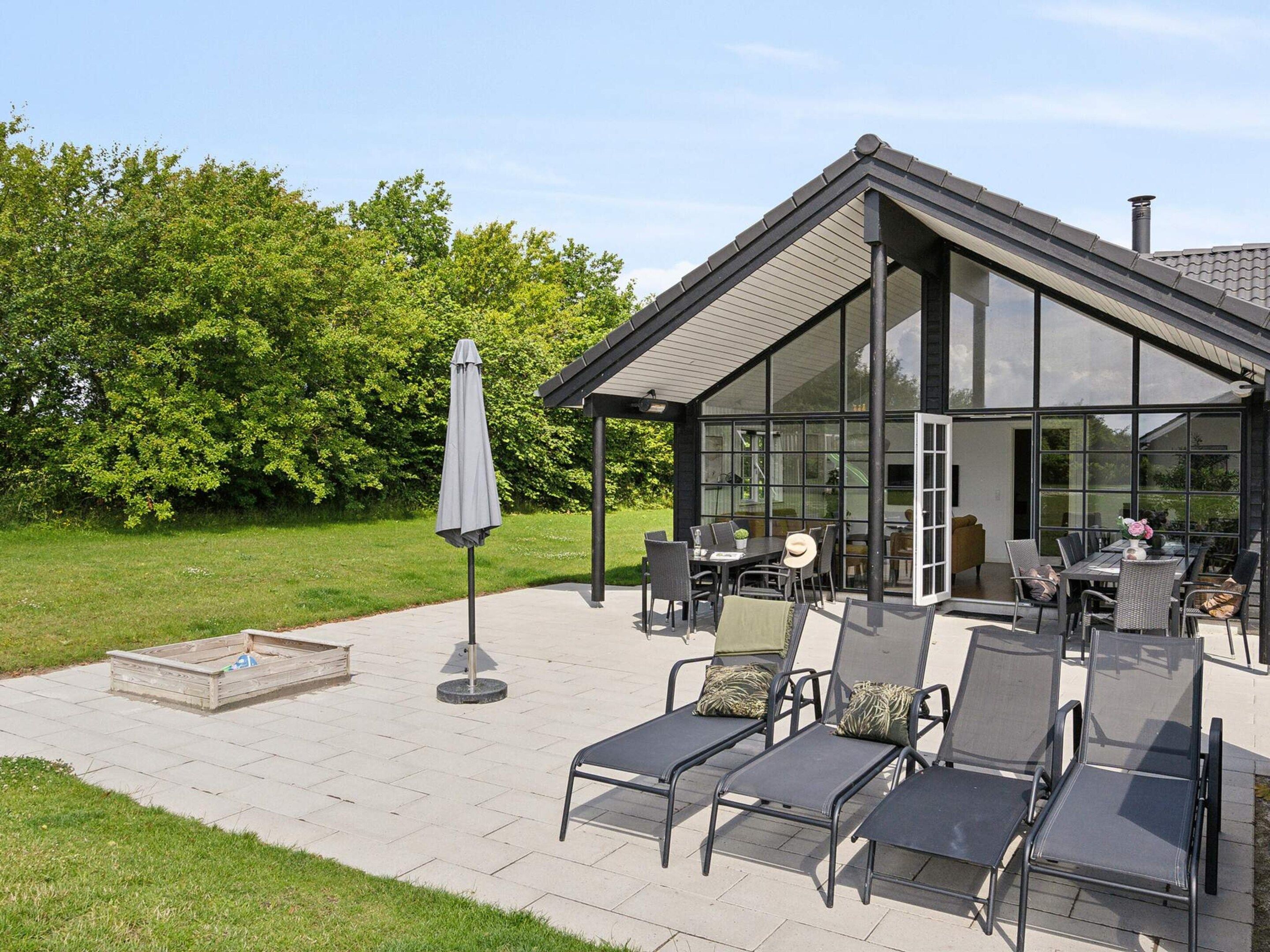 A modern outdoor patio with a glass enclosure, seating area, and a small table.