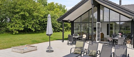 A modern outdoor patio with a glass enclosure, seating area, and a small table.