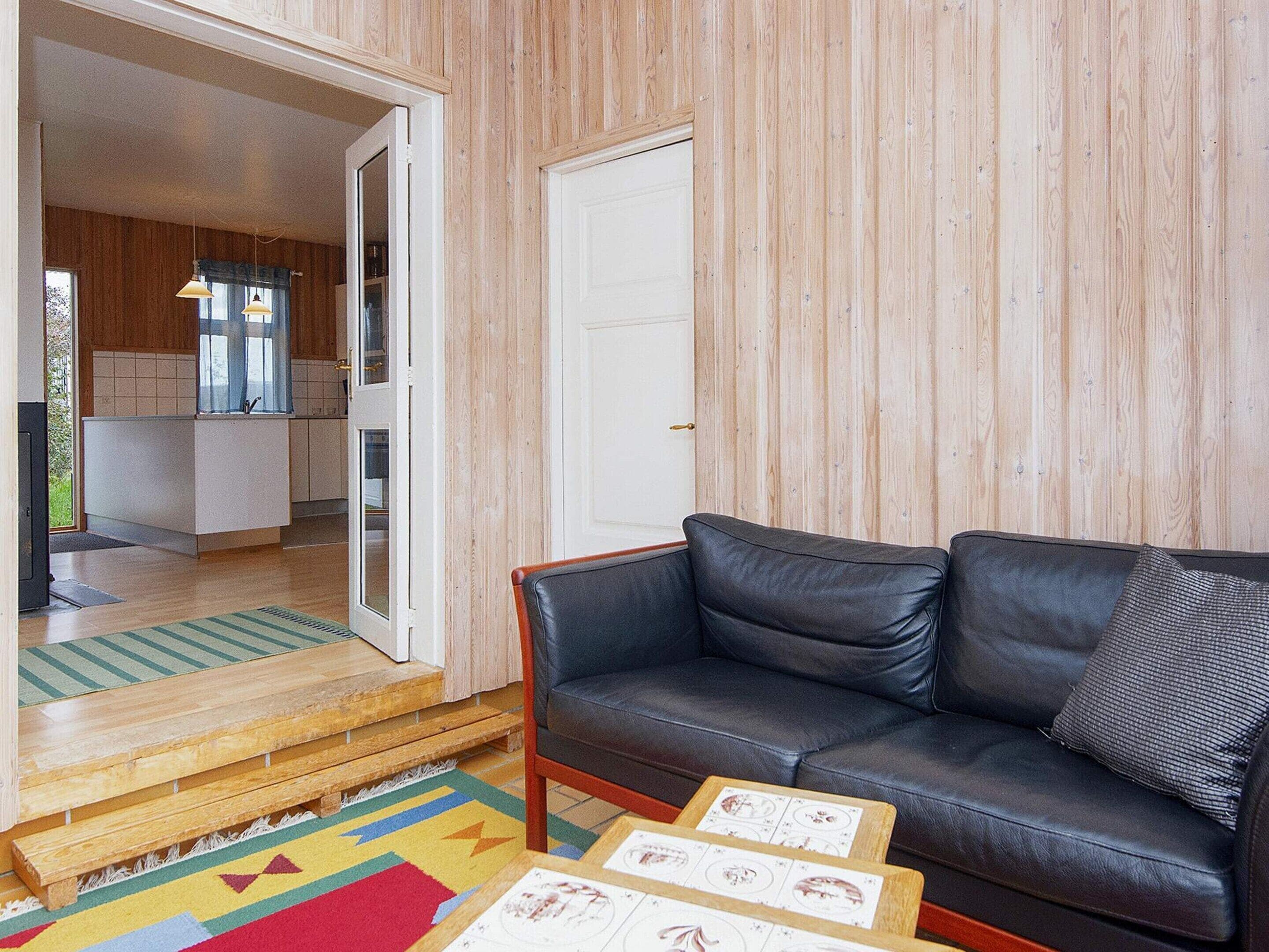 A modern living room with a leather sofa, a wooden coffee table with botanical prints, and a colorful rug.