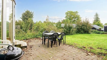 A patio with a table and chairs, a barbecue grill, and a glass greenhouse structure.