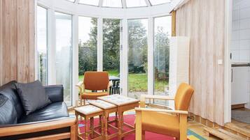 A conservatory with a glass ceiling, wooden furniture, and a view of the garden.