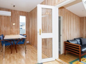 A room with a wooden paneled wall, a white door, a dining table with chairs, and a sofa.