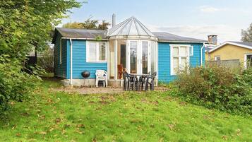 A house with a blue exterior, a glass conservatory, and a patio with a table and chairs.