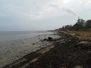 A coastal landscape with a rocky shoreline, a body of water, and a distant smokestack emitting smoke. - 4 Person Holiday Home in Ega (Aarhus)