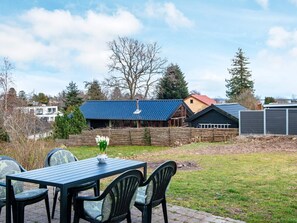 A patio with a table and chairs, a wooden fence, and a house with a blue roof in the background. - 4 Person Holiday Home in Ega (Aarhus)