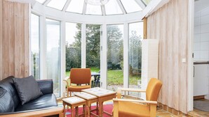 Une véranda dotée d’un toit en verre, de meubles en bois et offrant une vue sur le jardin.