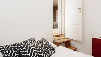 A bedroom with a bed, two patterned pillows, a white door, and a staircase leading to another room.