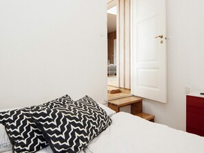 A bedroom with a bed, two patterned pillows, a white door, and a staircase leading to another room.