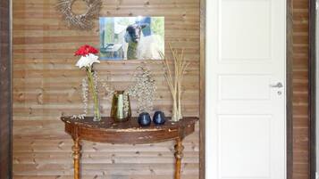 Una pared de madera con una puerta blanca, un arreglo decorativo, un cuadro enmarco y una pequeña mesa con jarrones y flores.