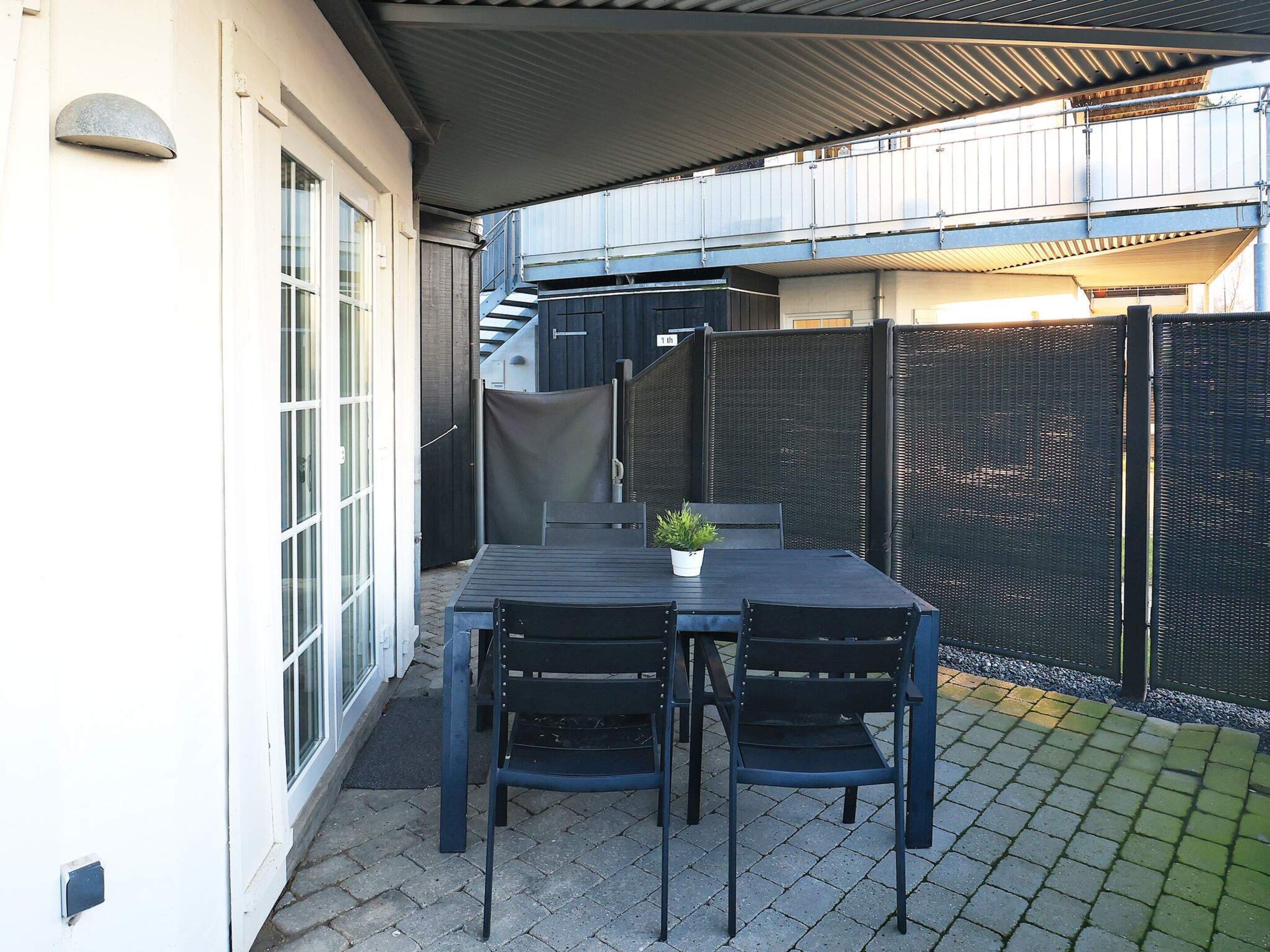 Eine Terrasse im Freien mit Tisch, Stühlen, einem Blumentopf und einem Metallzaun.