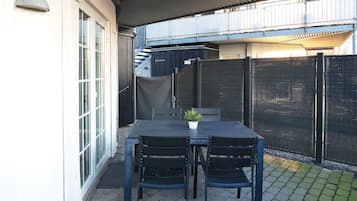 Eine Terrasse im Freien mit Tisch, Stühlen, einem Blumentopf und einem Metallzaun.