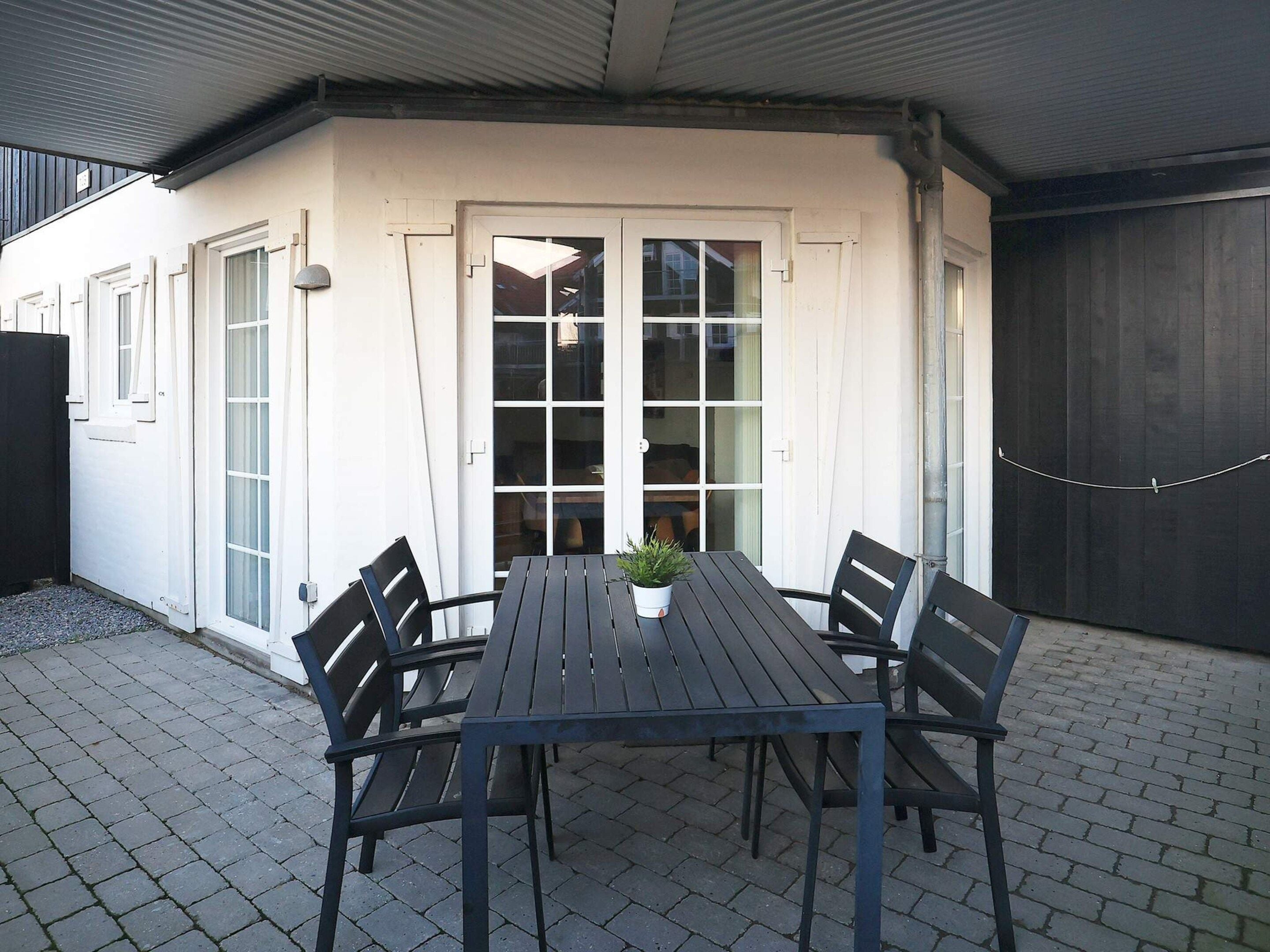 A patio with a table and chairs, a potted plant, and a sliding glass door leading to an interior space.